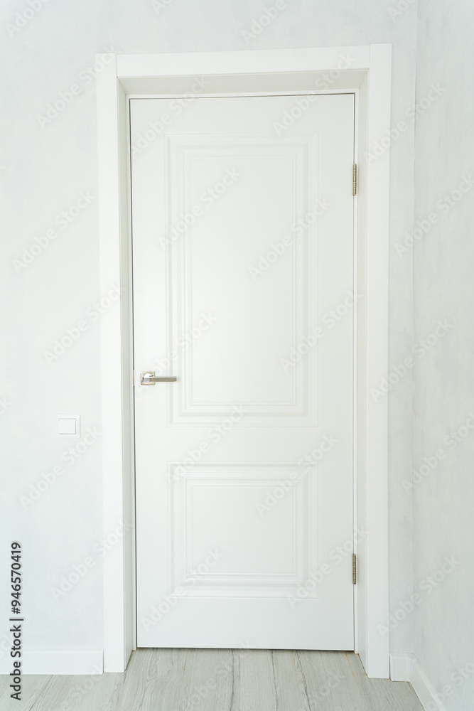 In a completely empty room characterized by white walls, there stands a white door that complements the wooden floor, creating a stark yet harmonious atmosphere for the space In a completely empty room characterized by white walls, there stands a white door that complements the wooden floor, creating a stark yet harmonious atmosphere for the space