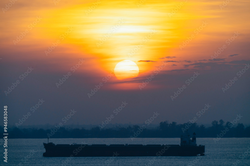 Fototapeta premium Cargo ship sailing on the sea against a sunset backdrop.