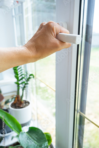 The hand holds the handle of a plastic double-glazed window, closing and opening the window with a rotary mechanism, the position of the handle for ventilation, micro-ventilation