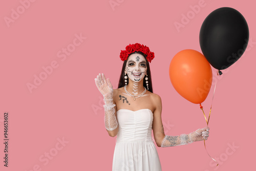 Beautiful young woman dressed as dead bride for Halloween party with balloons waving hand on pink background