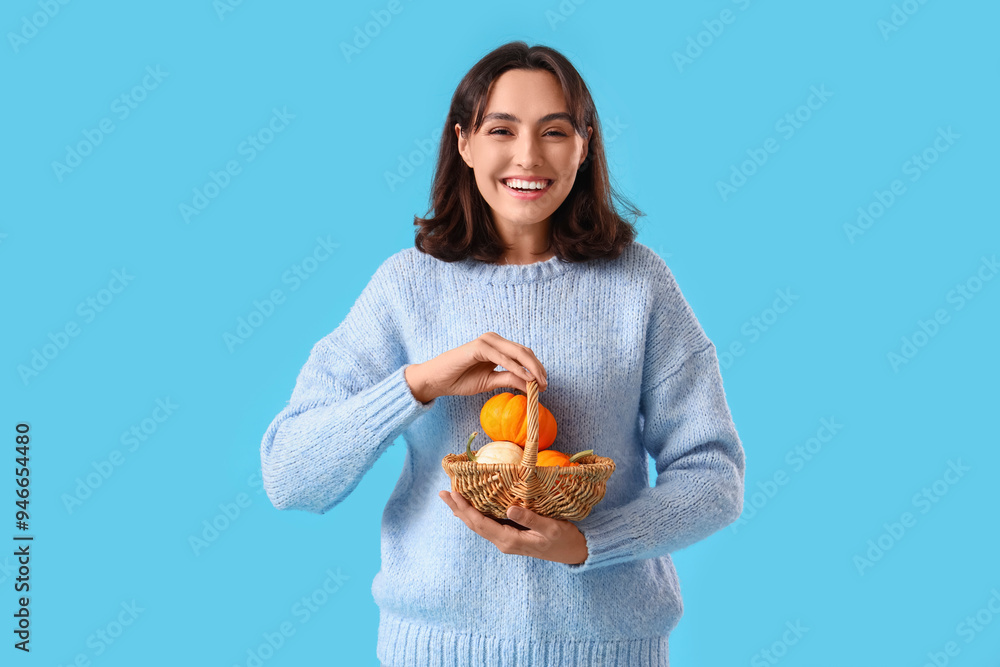 Young woman with wicker basket of pumpkins on blue background Young woman with wicker basket of pumpkins on blue background