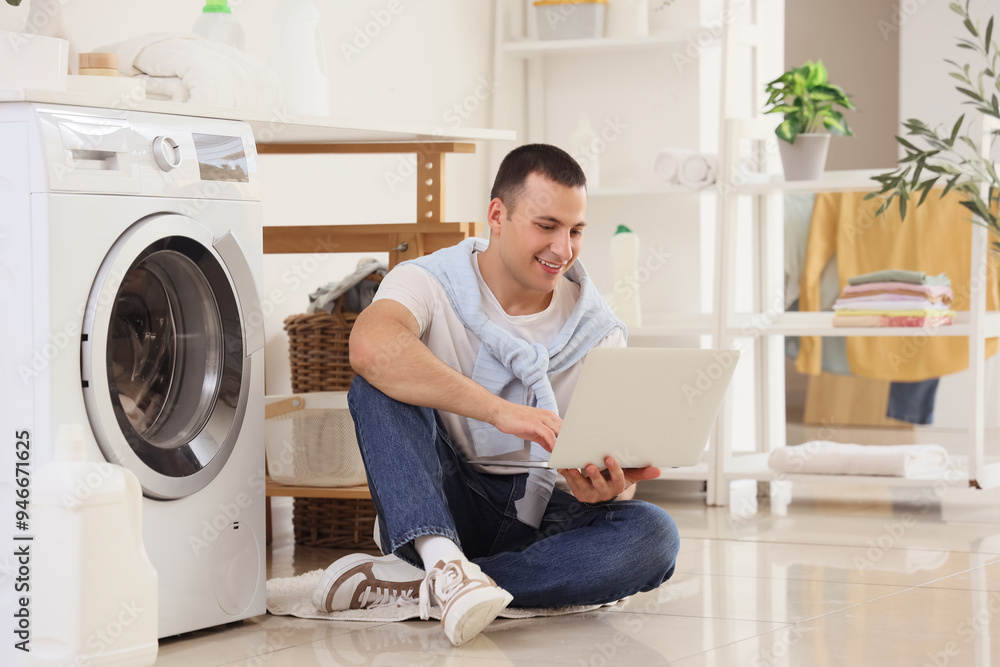 Young man using laptop near washing machine in laundry room Young man using laptop near washing machine in laundry room