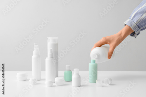 Woman pouring cosmetic product into travel bottle on light background