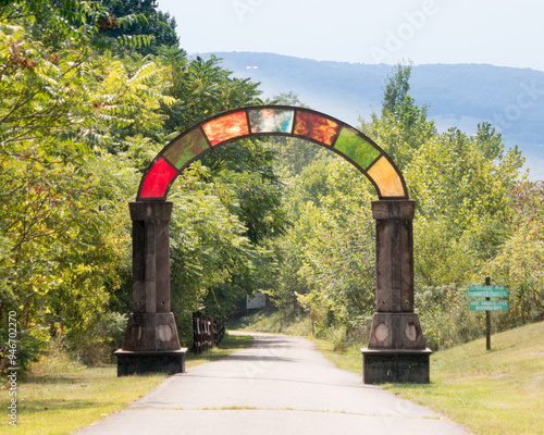 Fototapeta Naklejka Na Ścianę i Meble -  The Great Allegheny Passage rail trail showing colorful opalescent glass arch near Connellsville, PA, with mountain ridge in background