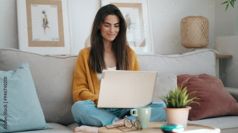 Video of beautiful young woman working with her laptop while sitting on a couch at home. Video of beautiful young woman working with her laptop while sitting on a couch at home.