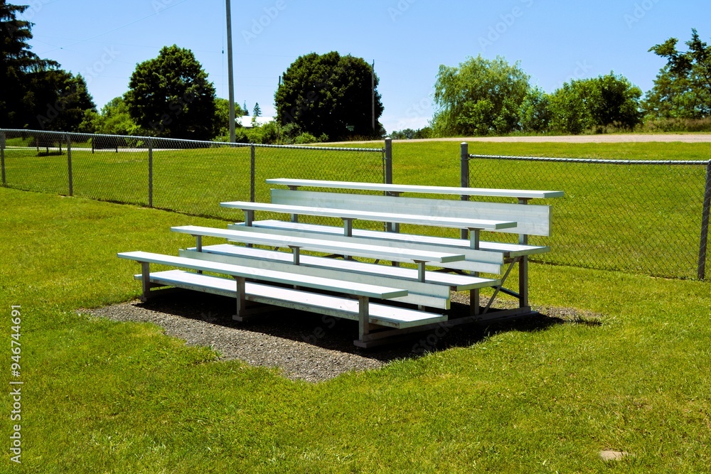 Aluminum bleachers sit empty at a soccer and sports field on a sunny summer day. Aluminum bleachers sit empty at a soccer and sports field on a sunny summer day.