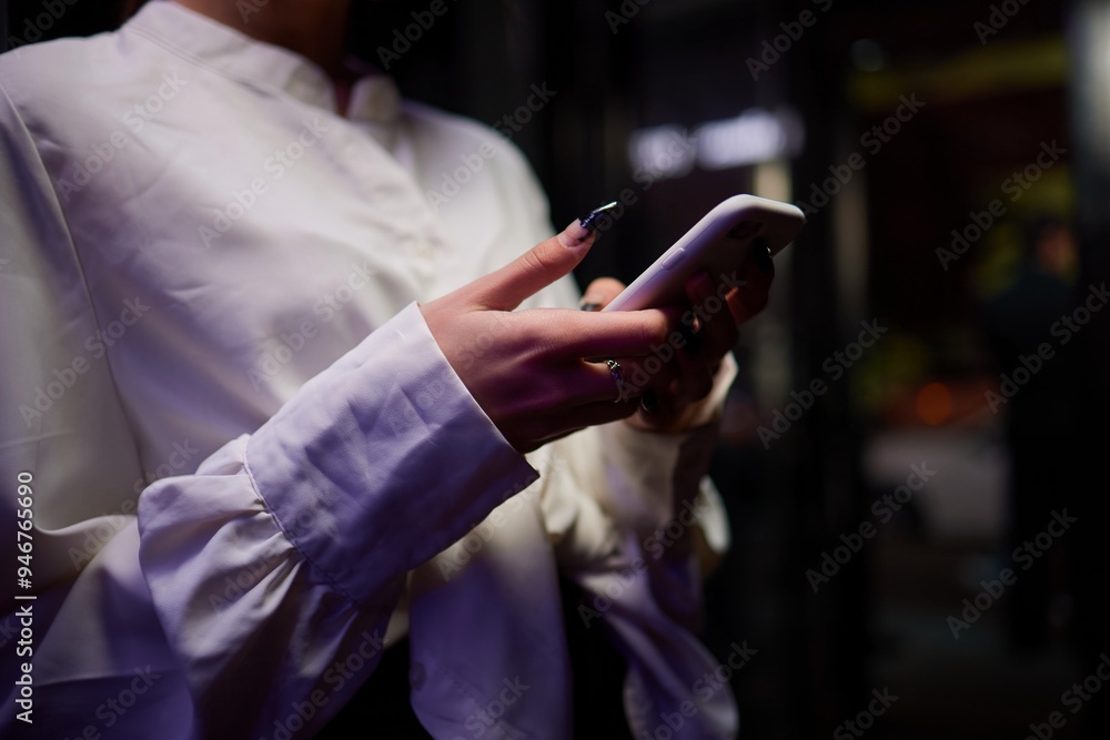 Woman in stylish dress with chic manicure using smartphone in closeup shot in nightclub Woman in stylish dress with chic manicure using smartphone in closeup shot in nightclub
