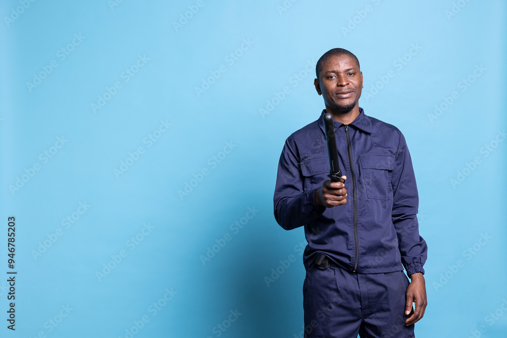 Male security agent posing with his police baton on camera, feeling proud about his responsibility against blue background. African american guard on duty, professional uniform. Male security agent posing with his police baton on camera, feeling proud about his responsibility against blue background. African american guard on duty, professional uniform.