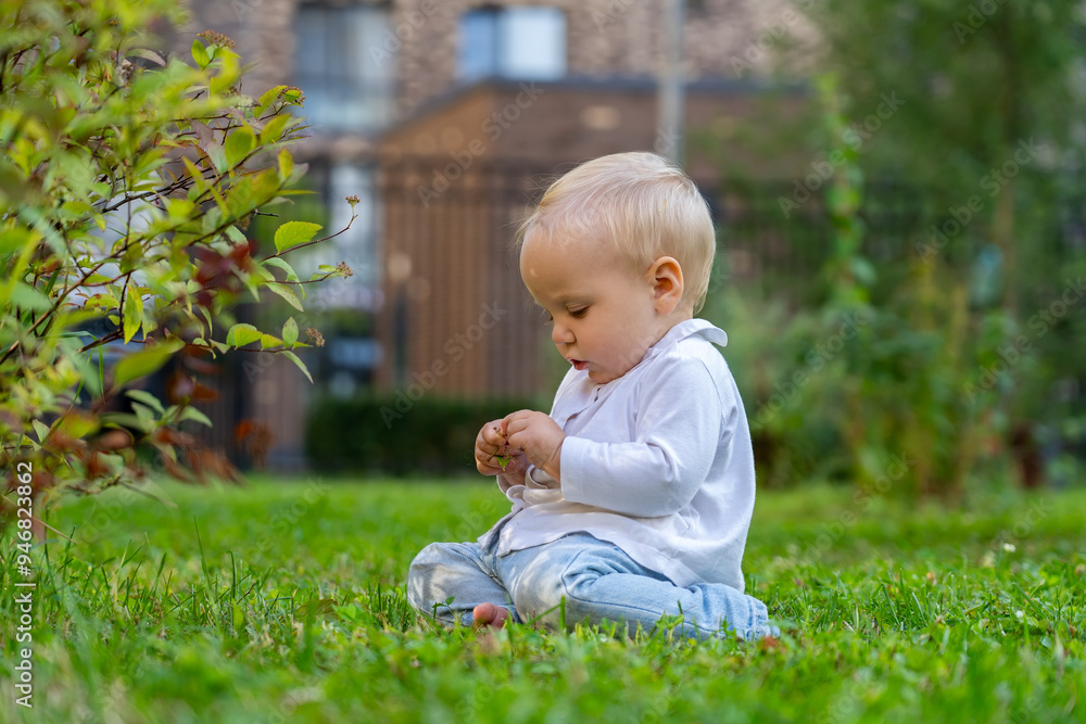 A little girl curiously examines a small object while seated on lush green grass in a peaceful garden A little girl curiously examines a small object while seated on lush green grass in a peaceful garden
