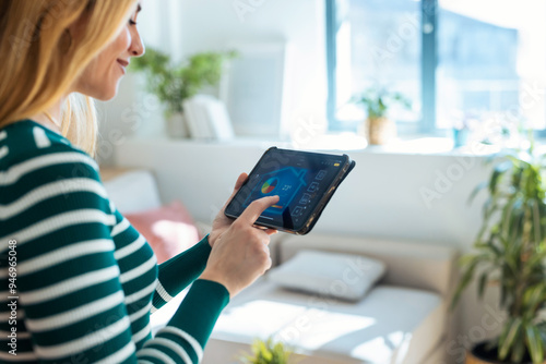 Fotografie Pretty young woman using the home automation system on digital tablet to regulate the temperature