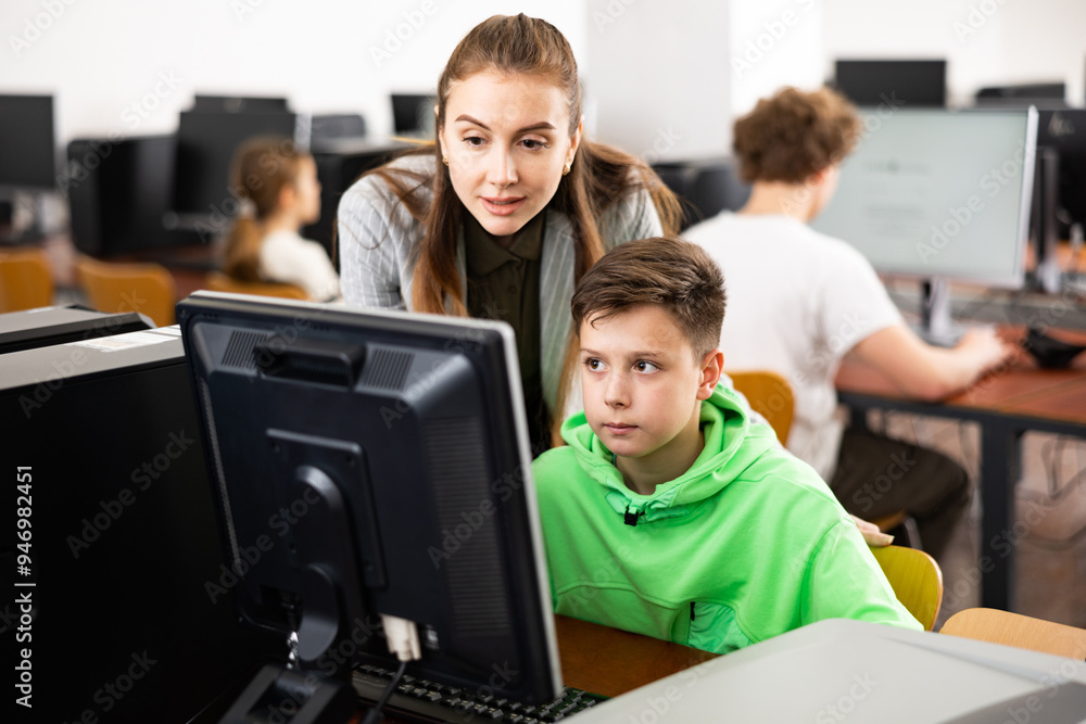 Fototapeta premium Teacher explaining task solution to teenage boy during computer science lesson in school.