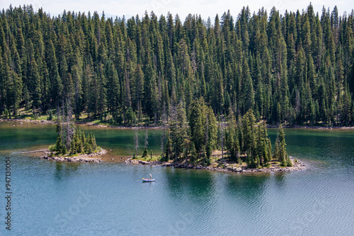 Fisherman angler in raft boat fishing near island in lake reservoir pine trees