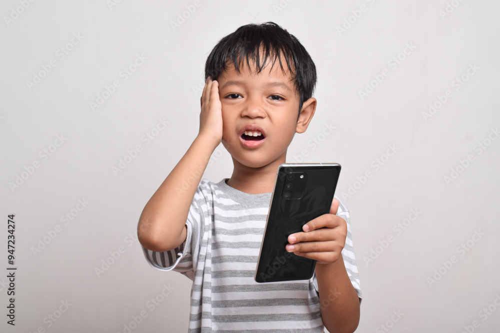 Sad Asian boy looking at smartphone with hand on head isolated on white background. little boy holding phone. he is shocked by what he sees. Sad Asian boy looking at smartphone with hand on head isolated on white background. little boy holding phone. he is shocked by what he sees.