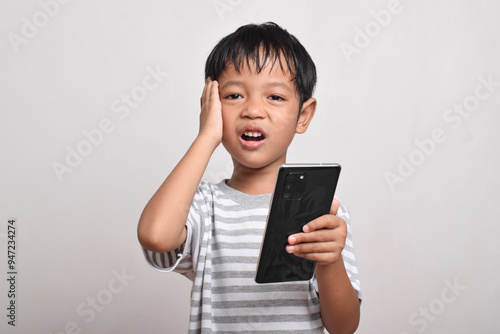 Sad Asian boy looking at smartphone with hand on head isolated on white background. little boy holding phone. he is shocked by what he sees.