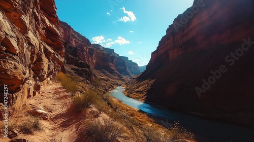 canyon landscape, deep red rock canyon with steep cliffs, a river winding through the canyon floor, clear blue sky with the sun casting deep shadows, layers of rock showing the passage of time, a photo