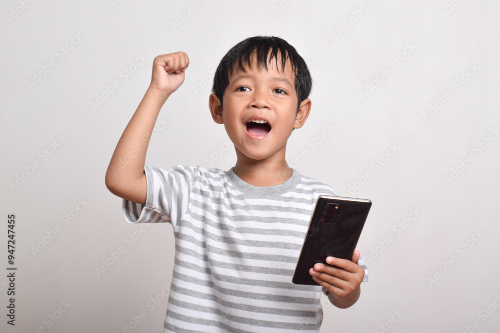 A happy and excited Asian boy with raised hand holding smartphone isolated on white background. little boy holding phone. Technology concept, copy space A happy and excited Asian boy with raised hand holding smartphone isolated on white background. little boy holding phone. Technology concept, copy space