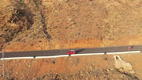 Aerial view of a scenic road with a red car winding through rocky terrain, Mirador de Las Penitas, Vega de Rio Palmas, Fuerteventura, Canary Islands, Spain. photo