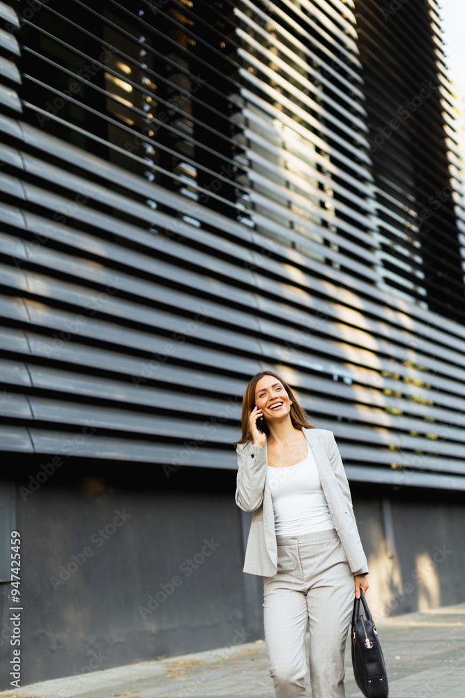 Confident business woman enjoying a sunny day while walking outdoors and chatting on the phone near a modern building Confident business woman enjoying a sunny day while walking outdoors and chatting on the phone near a modern building