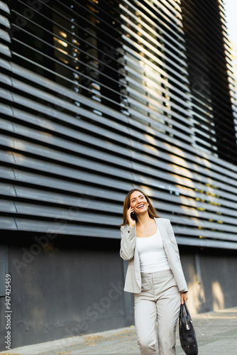 Confident business woman enjoying a sunny day while walking outdoors and chatting on the phone near a modern building