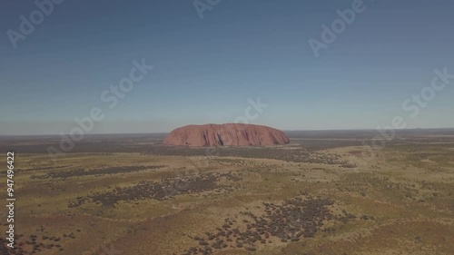 Aerial view of the iconic Uluru rock formation in a vast arid desert under a clear sky, Yulara, Australia.