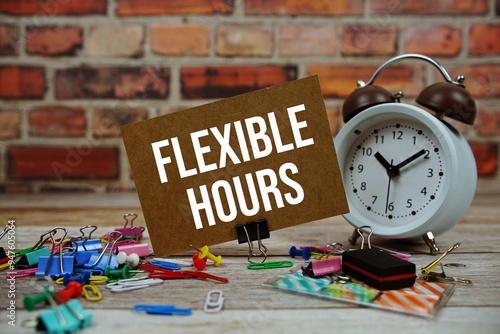 Flexible Hours text on paper card with alarm clock and stationary on wooden background photo