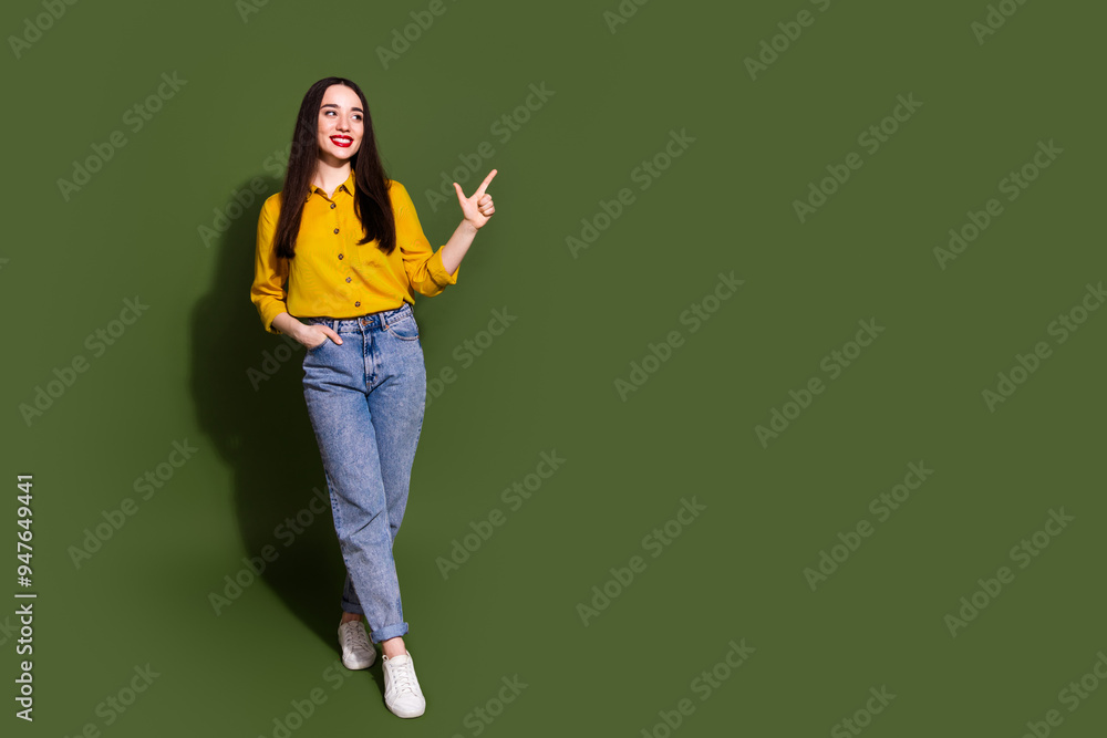 Full length photo of shiny attractive lady dressed yellow blouse pointing empty space isolated green color background Full length photo of shiny attractive lady dressed yellow blouse pointing empty space isolated green color background
