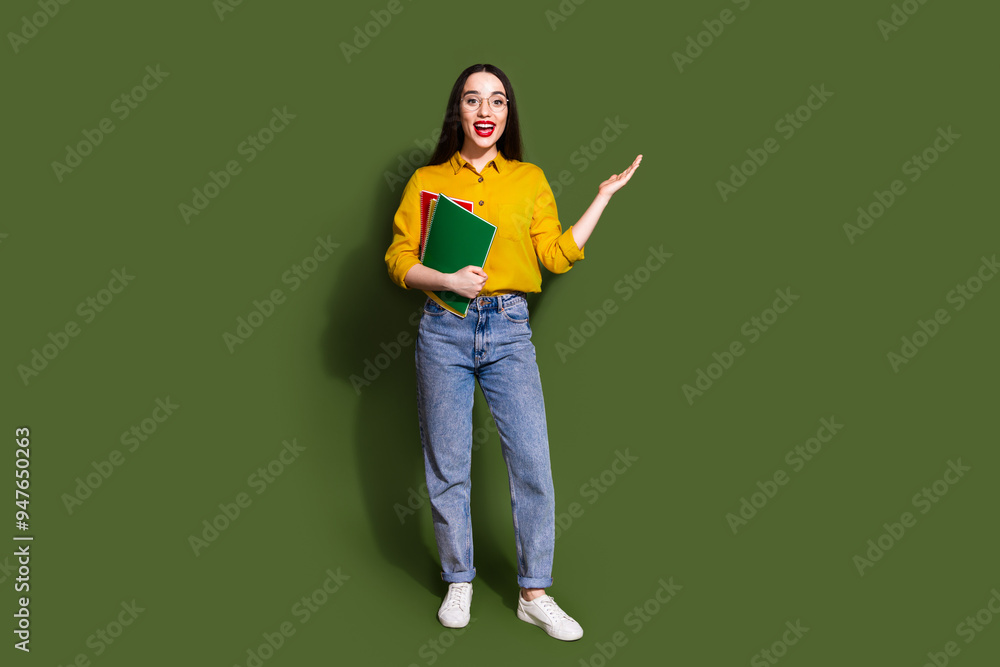 Full length photo of cheerful excited lady dressed yellow blouse rising arm holding book empty space isolated khaki color background Full length photo of cheerful excited lady dressed yellow blouse rising arm holding book empty space isolated khaki color background