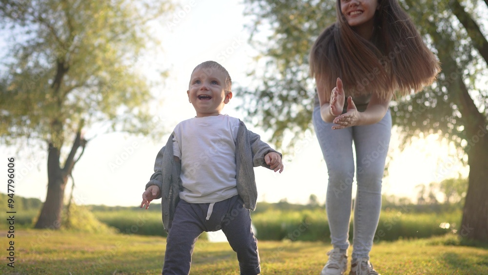 Fototapeta premium A baby is taking first steps in the grass. spring breastfeeding feet concept. a mom helps her baby with the first steps. lifestyle mom helps her baby with the first steps in the grass.