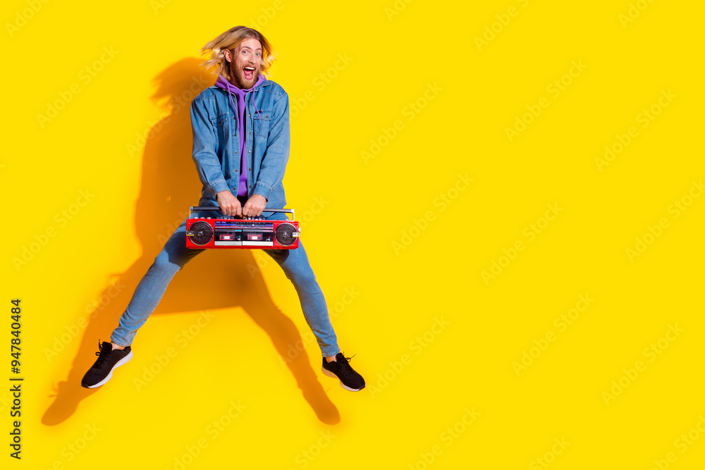 Full length portrait of nice young man boombox jump empty space wear denim jacket isolated on yellow color background Full length portrait of nice young man boombox jump empty space wear denim jacket isolated on yellow color background
