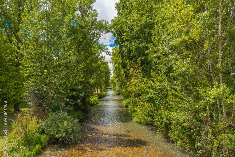 Tranquil view of the Arlanzon River surrounded by lush greenery in Burgos, Spain, on a sunny day Tranquil view of the Arlanzon River surrounded by lush greenery in Burgos, Spain, on a sunny day
