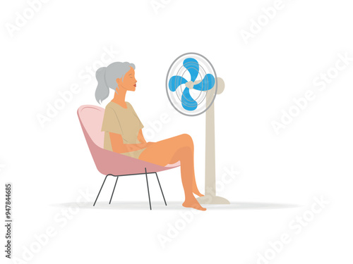A woman sits in a chair with a fan blowing on her. The woman is enjoying the cool breeze from the fan.Concept Menopause woman