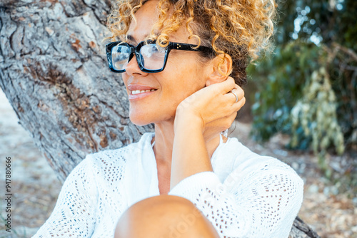 Canvas Print Smiling adult woman with curly hair updo and sunglasses gazes into the distance, expressing serenity and happiness while enjoying her leisure time alone in a park
