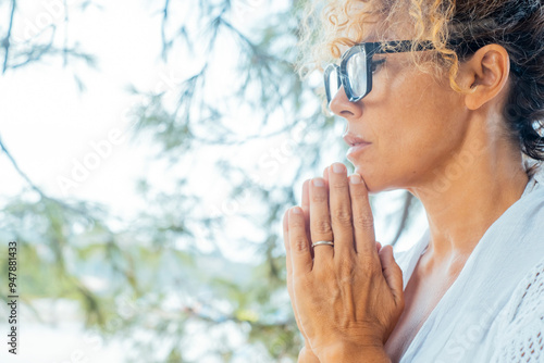 Side profile of a woman with hands clasped and eyes closed in a posture of prayer or meditation. Captures a serene and balanced mental state, embodying hope, healthy lifestyle, and zen discipline photo