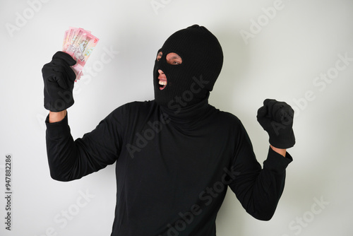 Dangerous young Adult black masked robber is holding a bunch of indonesian money after stealing from his victim. photo