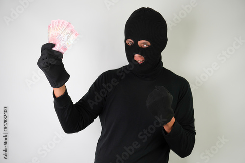 Dangerous young Adult black masked robber is holding a bunch of indonesian money after stealing from his victim. photo