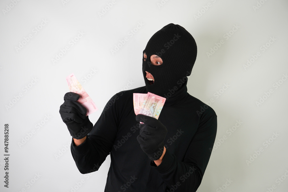 Dangerous young Adult black masked robber is holding a bunch of indonesian money after stealing from his victim. Dangerous young Adult black masked robber is holding a bunch of indonesian money after stealing from his victim.