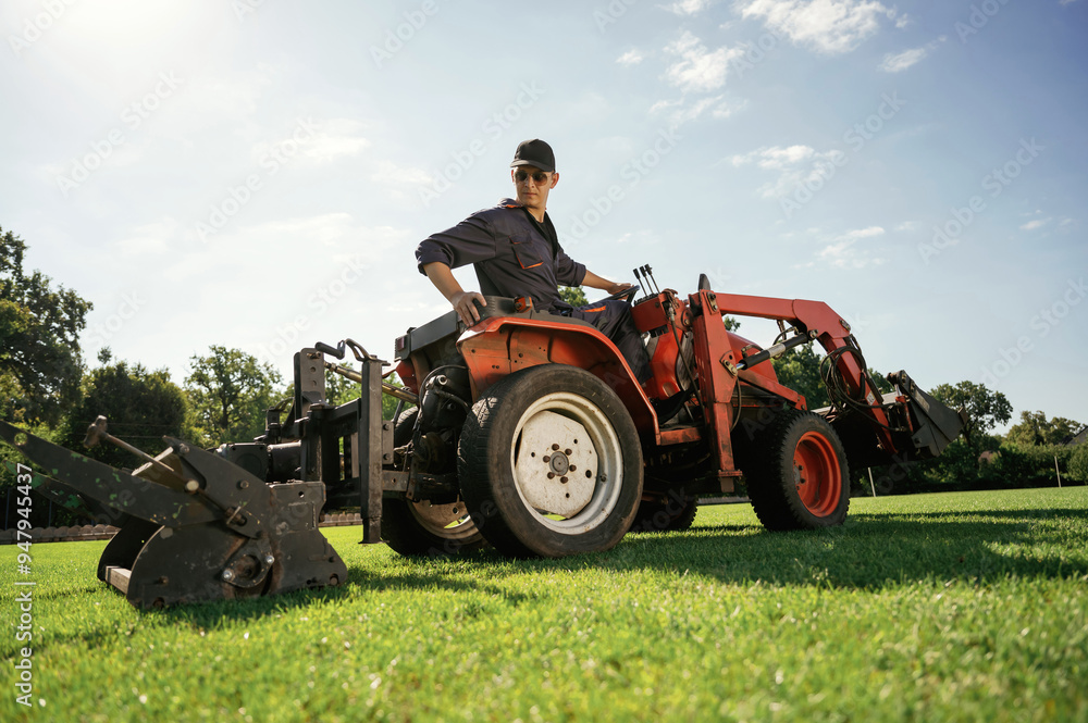 Obraz premium Loan work. Man is with utility tractor with grass cutter and aerator equipment on the field