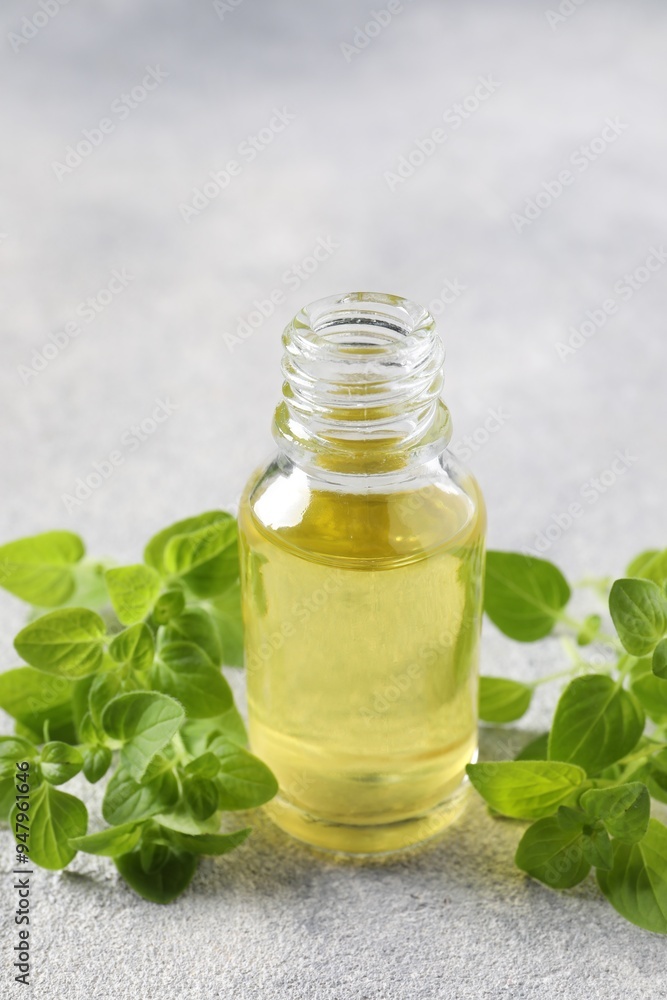 Essential oil in bottle and oregano leaves on light grey textured table, closeup Essential oil in bottle and oregano leaves on light grey textured table, closeup