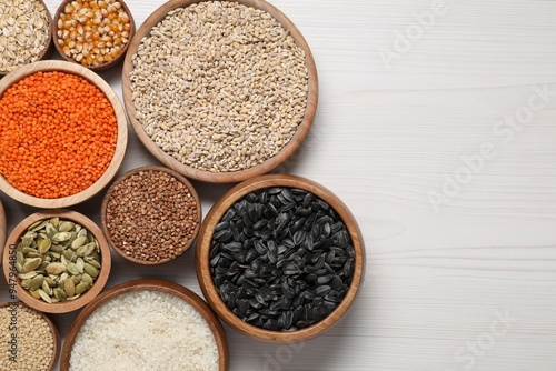 Different types of cereals, seeds and legumes in bowls on white wooden table, flat lay. Space for text