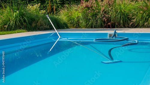 A pool cleaning hose and skimmer in a clear blue pool, surrounded by lush greenery, emphasizing pool maintenance.