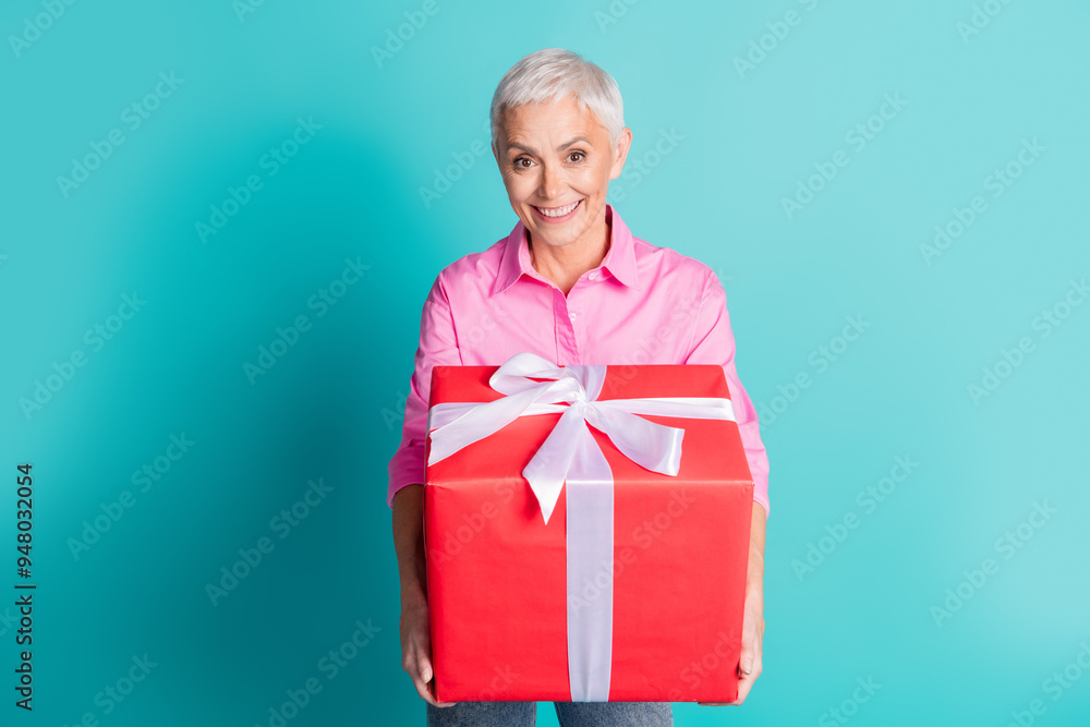 Portrait of pretty aged lady hold giftbox wear pink shirt isolated on turquoise color background Portrait of pretty aged lady hold giftbox wear pink shirt isolated on turquoise color background