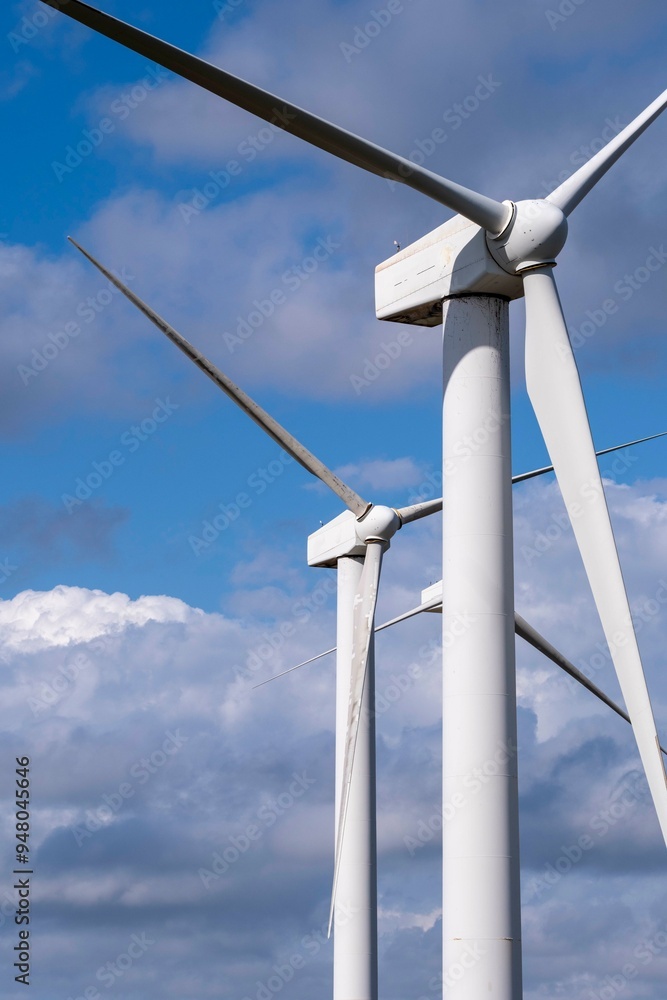 Pair of towering wind turbines reaching high into a vibrant blue sky, surrounded by light fluffy clouds, symbolizing progress and the use of clean, renewable energy in Tarragona Spain Pair of towering wind turbines reaching high into a vibrant blue sky, surrounded by light fluffy clouds, symbolizing progress and the use of clean, renewable energy in Tarragona Spain