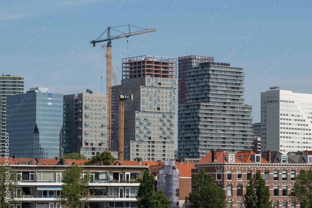 A vibrant scene showing mid-rise buildings under construction with prominent cranes highlighting development and urban growth set against a clear blue sky in Rotterdam Netherlans A vibrant scene showing mid-rise buildings under construction with prominent cranes highlighting development and urban growth set against a clear blue sky in Rotterdam Netherlans