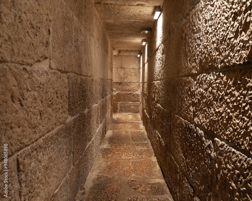 narrow stone corridor in a castle, pyramid or church with lighting
