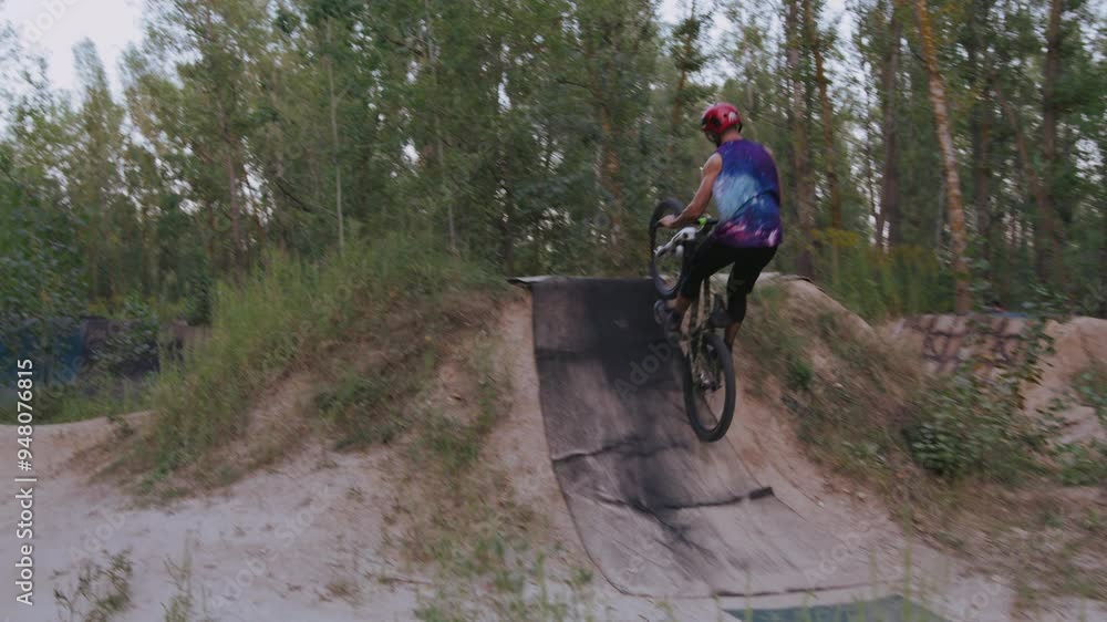 Dirtbiker in headwear doing two high jumps in wooded area Dirtbiker in headwear doing two high jumps in wooded area