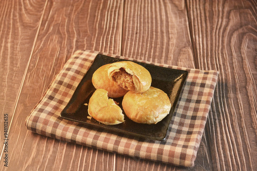 Chinese Pastry Mooncake baked round asian crispy cake with salted yellow red bean paste and eggs yolk in black plate on wood table Traditional halal menu food sweet dessert for autumn festival cafe