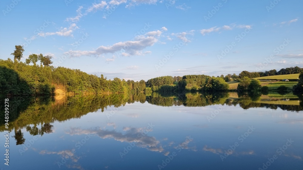 A tranquil lake perfectly reflecting the trees in a serene and picturesque landscape A tranquil lake perfectly reflecting the trees in a serene and picturesque landscape