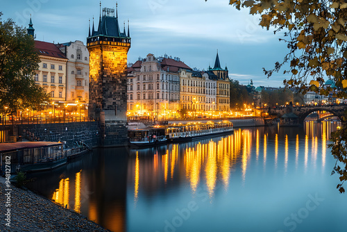 Sitkov Water Tower and the Vltava Embankment in Prague, Czechia. The historic water tower stands tall against a backdrop of brightly lit buildings lining the riverbank. Prague dusk picturesque photo