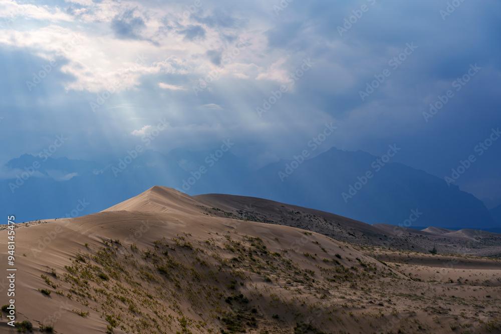 Sunlit desert dunes under dramatic clouds and sunbeams Sunlit desert dunes under dramatic clouds and sunbeams