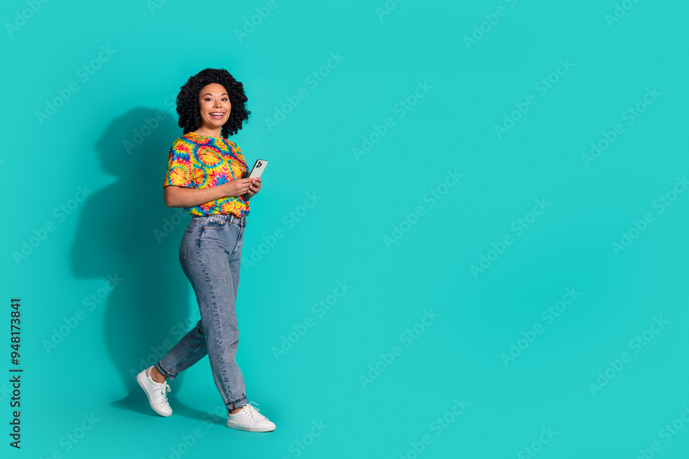 Full length photo of adorable lovely girl wear print t-shirt walking communicating modern device empty space isolated turquoise color background Full length photo of adorable lovely girl wear print t-shirt walking communicating modern device empty space isolated turquoise color background